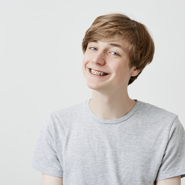Jugendlicher mit Zahnspange lächelt in die Kamera – kieferorthopädische Behandlung für gerade Zähne und ein gesundes Lächeln.